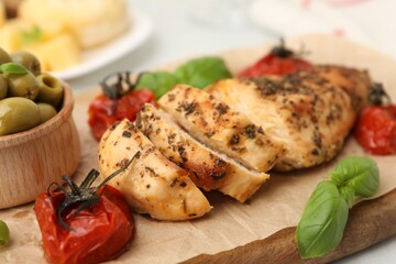 Serving board with fried chicken breast, sun dried tomatoes, basil and olives on light table, closeup