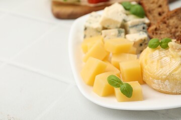 Different types of cheese, bread and basil on light tiled table, closeup. Space for text