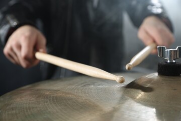 Man with drumsticks playing cymbal on black background, closeup