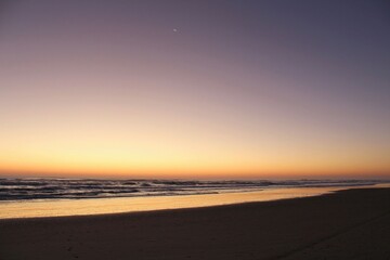 Obraz premium Peaceful Ocean Sunset with Crescent Moon and Gentle Waves