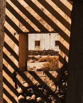 Juego de luces y sombras proyectadas sobre una estructura en ruinas, creando patrones geom&eacute;tricos y una atm&oacute;sfera c&aacute;lida y misteriosa en un entorno arquitect&oacute;nico abandonado.