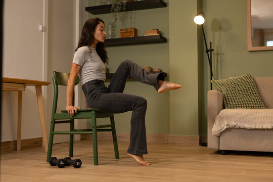 Athletic woman performing seated core exercise on chair at home using bodyweight training to improve balance stability and lower body strength during indoor fitness workout