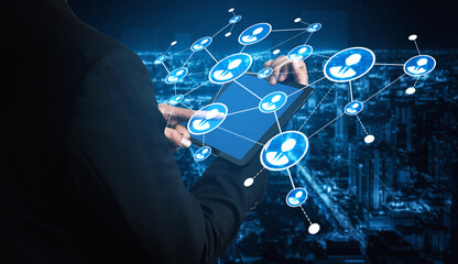 A businessman interacts with a tablet, creating a digital network over a vibrant city skyline at night, showcasing modern technology and connectivity concepts. Tessel