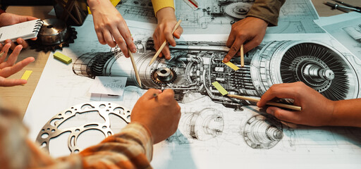 A vibrant scene capturing hands engaged in a collaborative workshop focused on mechanical engineering design, with blueprints and technical drawings laid out for discussion. SACTR