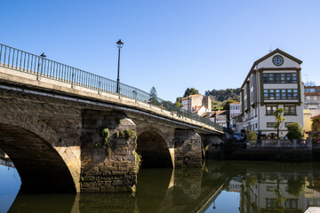 Obraz premium Scenic view of Ponte Vella bridge over Mandeo River in Betanzos, Galicia, Spain, surrounded by lush greenery and historic architecture.