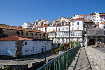 Fototapeta premium Traditional Galician white buildings seen from Ponte Vella bridge over Mandeo River in Betanzos, Spain, surrounded by lush greenery.