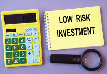 LOW RISK INVESTMENT - words in a notebook with a calculator and magnifying glass in the background
