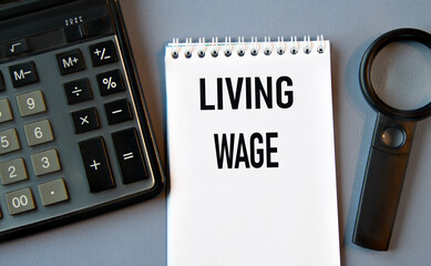 LIVING WAGE - words in a notebook with a calculator and magnifying glass in the background