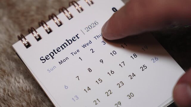 Close-up of September 2026 calendar page with finger pointing at date, planning and organization concept.