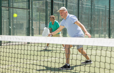 Naklejka premium Elderly man and adult man in doubles playing paddle tennis on tennis court