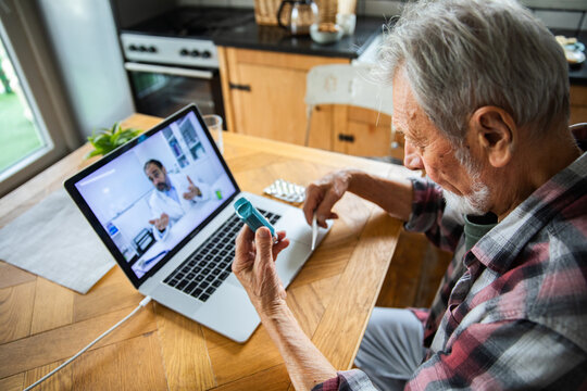 Senior man showing inhaler during online doctor consultation at home
