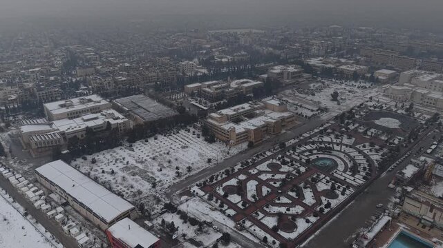 A drone shot of Aleppo, Syria, during a heavy snowstorm shows urban architecture and streets covered in white. Cinematic winter scenery in a Middle Eastern urban environment.