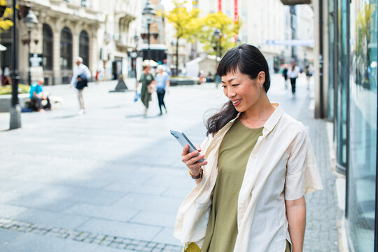 Smiling woman using smartphone on city street outdoors