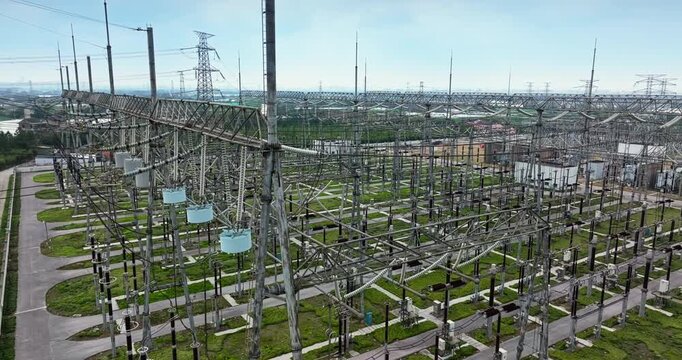 Industrial electrical substation with high voltage power lines and transformers in an open field under a bright sky.