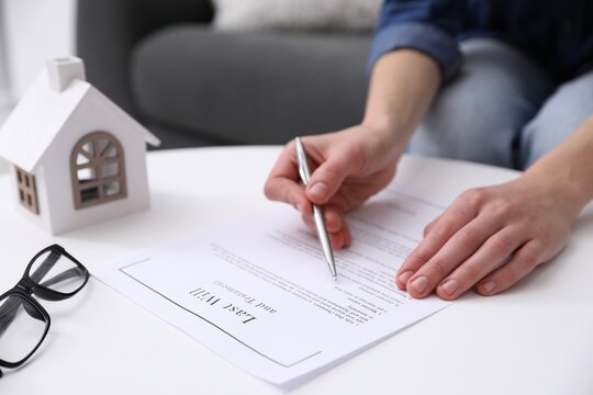 Woman signing Last Will and Testament at white table indoors, closeup