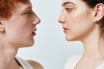 Portrait of young man and woman facing each other with calm expression closeup on light background, showing natural skin and facial features in detail.