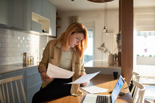 Woman reviewing bills at kitchen table with laptop