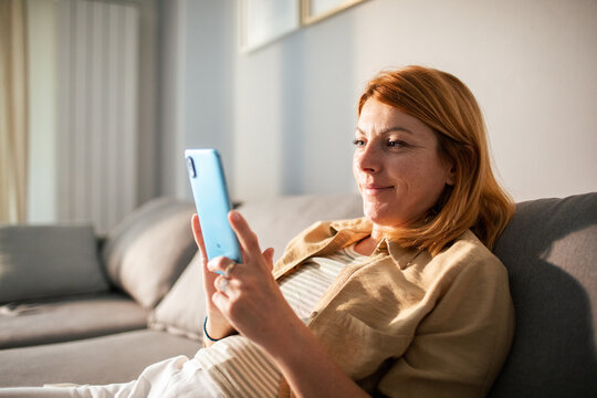 Smiling woman using smartphone on sofa at home