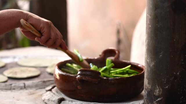 Mexican woman's hands stirring traditional food in a clay pot, preparing chopped prickly pear.