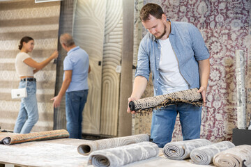 Young man buyer choosing soft rolled carpet in hardware store