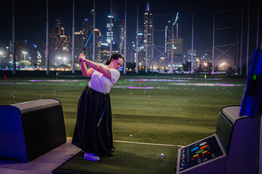 Woman golfing at Topgolf Dubai with city skyline illuminated at night, showcasing vibrant lights and modern architecture in the background