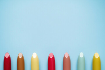 Colorful lipstick tube tops arranged in a row on blue background highlighting cosmetics variety and makeup color choice.