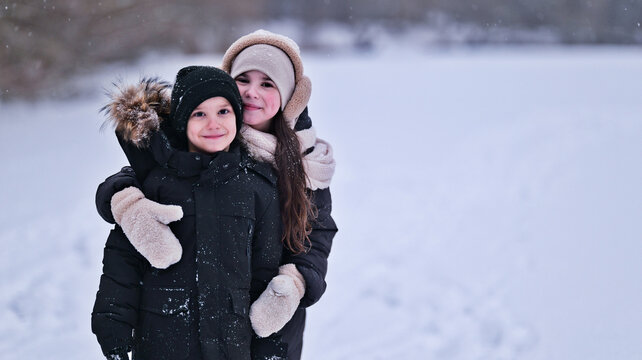 Two happy children in winter coats embracing in a snowy landscape