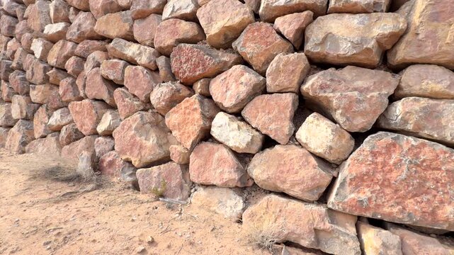 Pan shot of dry stack wall construction for retaining soil and stone material in arid environment of rugged desert terrain