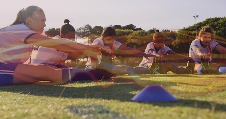 Stretching five teammates reaching toward feet on grassy field, in team kit, with blue cone