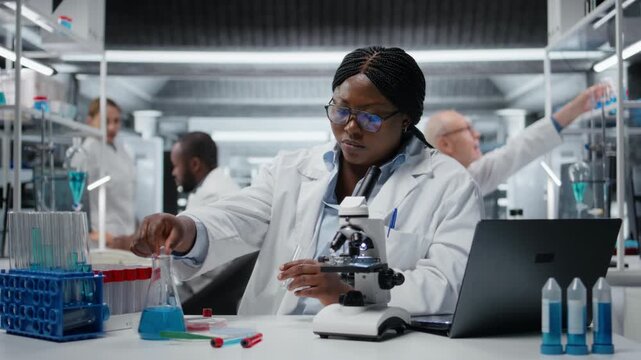 Clinical laboratory technologist pipetting reactant into blue solution for purity analysis. African american woman adding liquid agent to test tube to observe chemical reaction properties, camera A