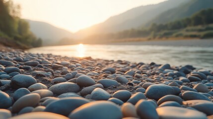 Fototapeta premium Smooth grey river stones forming a subtle mosaic pattern on a serene beach with mountains and golden sunset in the background