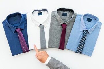 Obraz premium Four men's dress shirts with ties: blue with polka dot tie, white with gray tie, gray with burgundy tie, light blue with striped tie. Hand pointing at shirts. Men's fashion, top view.