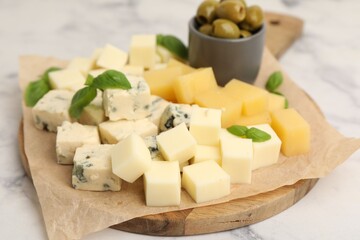 Serving board with different types of cheese, olives and basil on light marble table, closeup