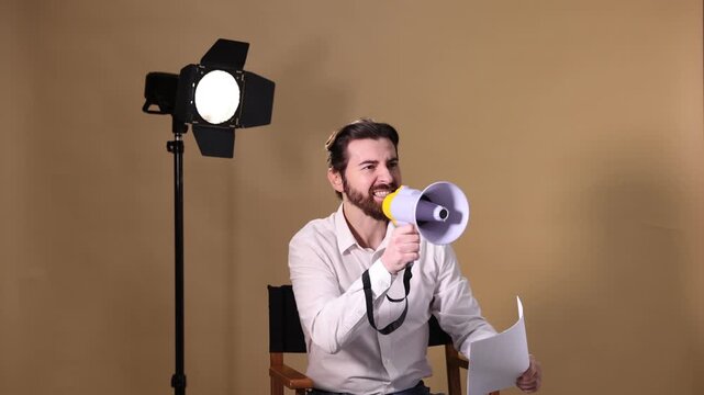 Film director with script and megaphone on chair against beige background
