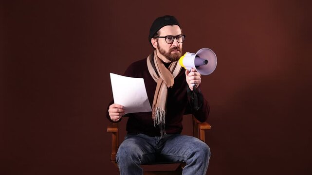 Professional film director with megaphone and script on chair against brown background