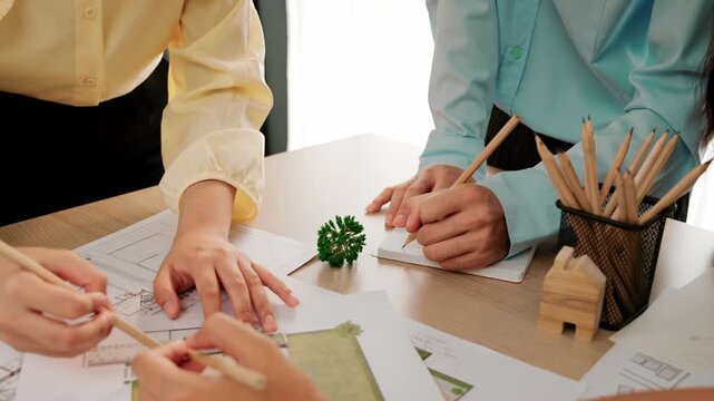 Smart architect and safety engineer discussion about building blueprint on table with architectural document, measurement tools and wooden block scatter around at modern office. Closeup. Delineation.
