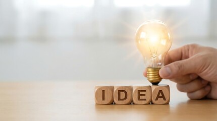 Hand holding glowing light bulb over wooden idea blocks on desk with soft lighting for creativity and innovation concept