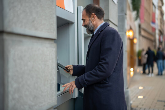 Mature man using atm with smartphone for transaction