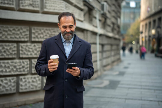 Happy man smiling using smartphone drinking coffee on street - Powered by Adobe