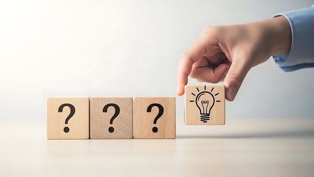 Hand placing lightbulb idea block among question mark wooden cubes on table