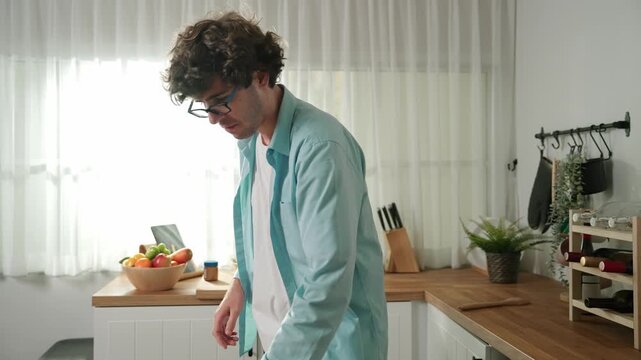 Happy father move to music while cooking food and prepare lunch at modern kitchen. Active dad dancing to song while making healthy food or salad surrounded with vegetable and kitchenware. Pedagogy.