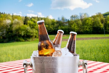 Beer bottles chilling in ice bucket on picnic table in sunny outdoor setting. © Kittiphan
