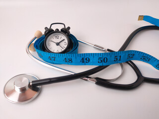 The image displays a&nbsp;stethoscope, a measuring tape, and a small alarm clock on a white background