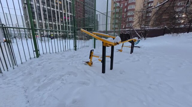 Outdoor fitness equipment covered with snow in residential area showing winter season inactive public sports infrastructure and urban lifestyle