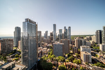 Obraz premium Toronto cityscape showcasing a panoramic perspective of numerous high rise residential and commercial skyscrapers under a clear blue sky, surrounded by green urban foliage