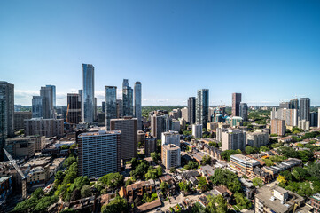 Obraz premium Toronto cityscape with towering skyscrapers, high rise residences and tree lined streets under a clear blue sky, showcasing vibrant urban development and skyline views