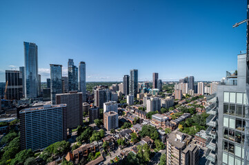 Obraz premium Toronto's urban landscape blends modern high rise architecture with residential neighborhoods and green spaces under a clear blue sky, illustrating city growth and diverse living environments