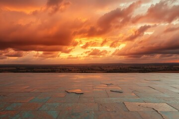 Weathered paving stones reflect the vivid orange and deep gray clouds of a sunset sky which stretches above a blurred expansive distant landscape