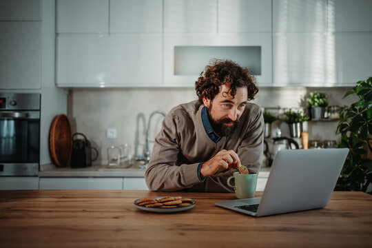 Man enjoying snack and coffee while working on laptop
