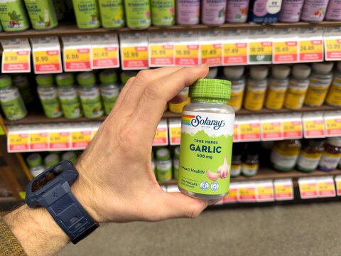 Hand Holding Solaray Garlic Supplement Bottle On Vitamin Store Shelf